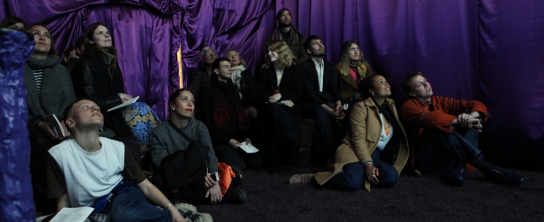 Personer sidder på tæppe på gulv i rum med stofbeklædte vægge