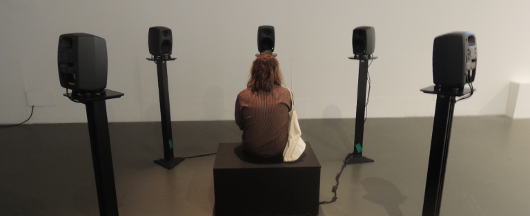 Person sidder på kasse omgivet af fem højtalere