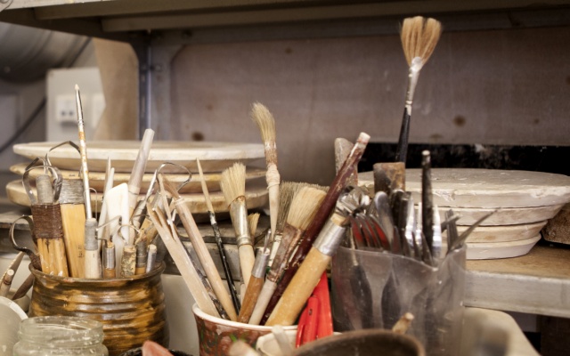 Pensler og andre redskaber i krus foran stablede gipsplader