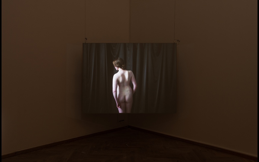 Installationsfoto af Luna Emilie Printz Scales' afgangsværk Eyelids (skærm med nøgen kvinde på plint som drejes af to personer)