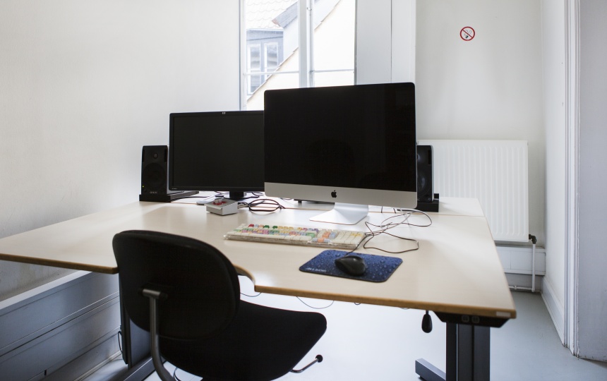 Rullestol foran bord med computer, tastatur og computermus, monitor og højtalere